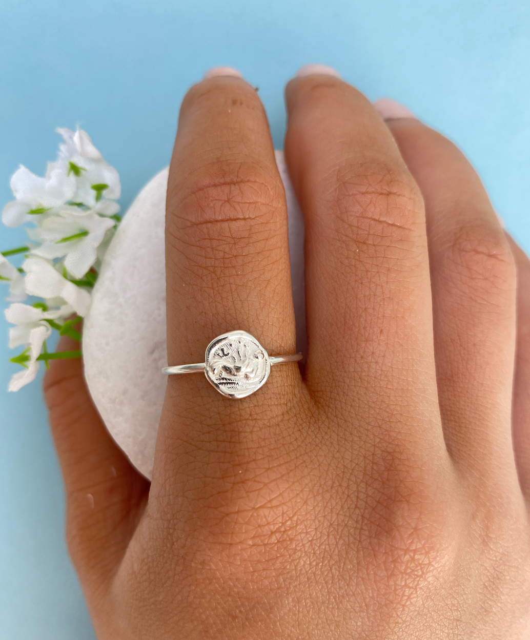 A silver ring with a sea animal design set onto a circular motif is worn on a hand
